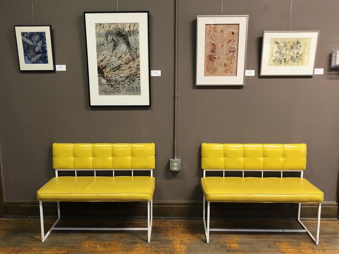 Photograph of two yellow chairs in a gallery with four photos on the wall